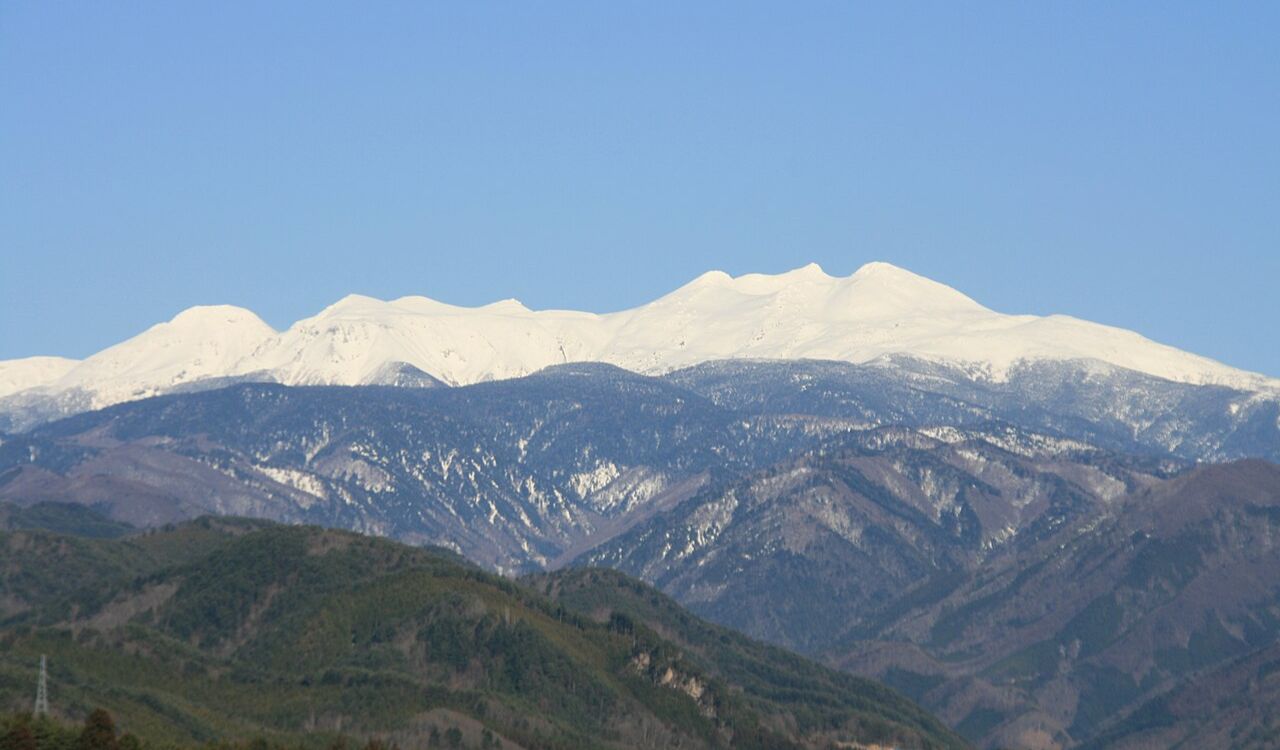 Snow-capped peaks of Mount Norikura with surrounding green hills in Japan