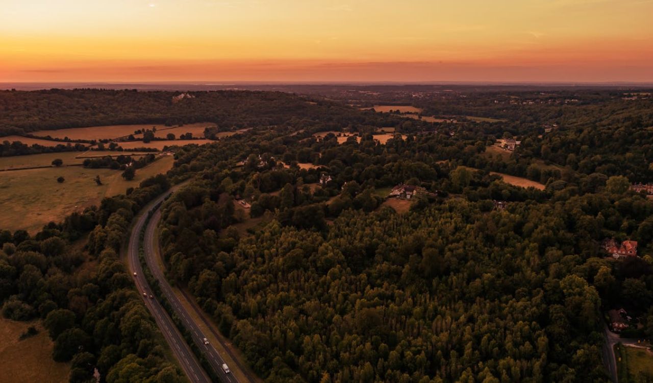 A winding road cuts through golden New England forests at sunset, perfect for a cozy fall road trip