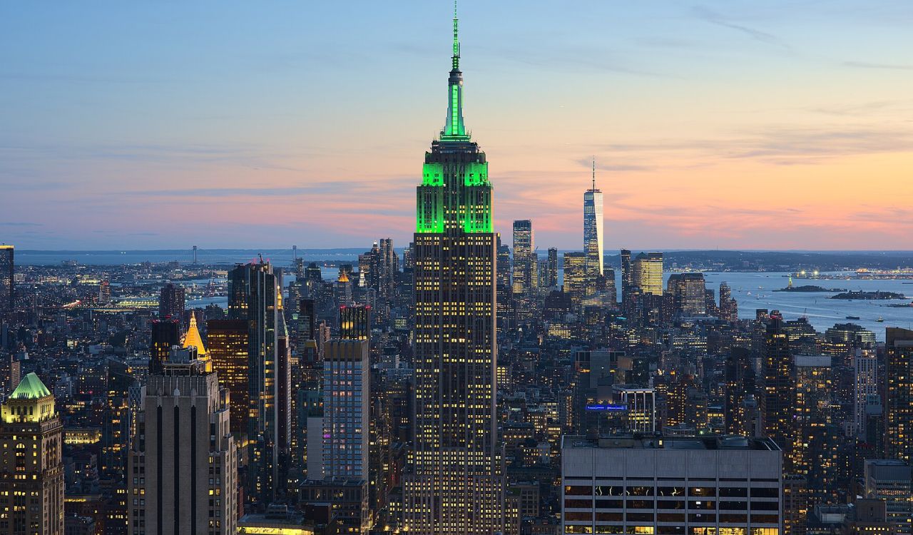 Empire State Building glowing green at sunset above the Manhattan skyline and Hudson River