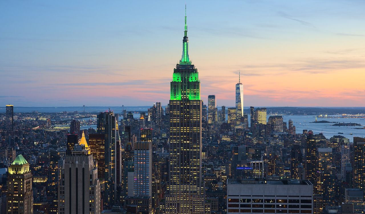 Empire State Building illuminated in green at sunset, with the New York City skyline in the background
