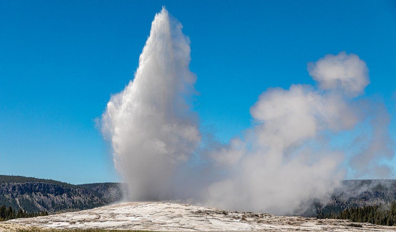Old Faithful geyser erupting in Yellowstone National Park under blue sky