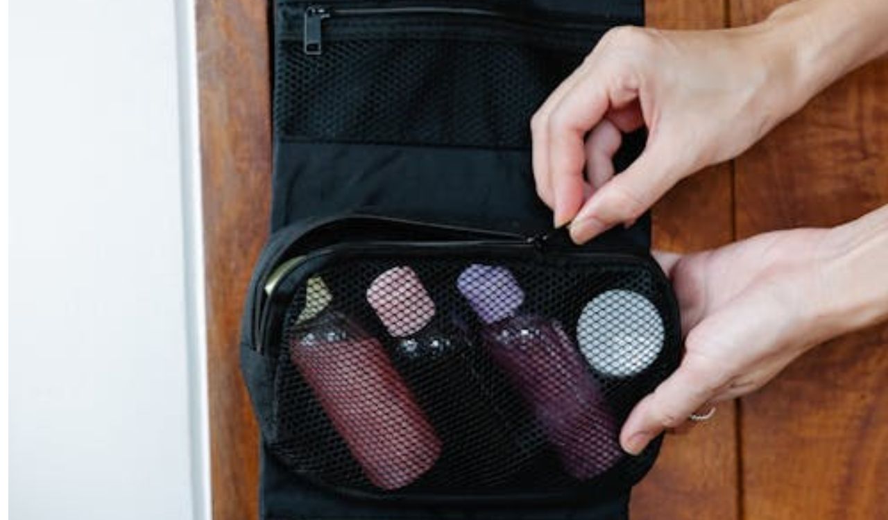 A person holding a toiletry bag hanging on a door, with bottles and toiletries neatly arranged inside