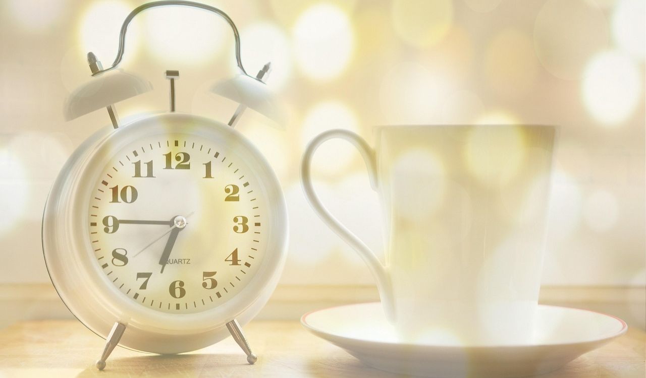 A vintage-style alarm clock with a cup and saucer, creating a warm, cozy scene with a soft bokeh background