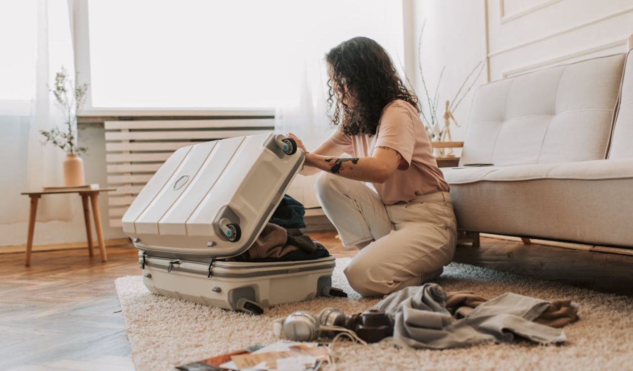 Young woman kneeling on floor while packing clothes into a suitcase in a cozy, well-lit living room