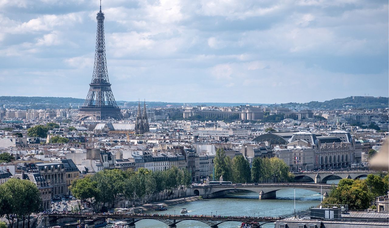 A stunning view of the Eiffel Tower in Paris, with the Seine River and iconic bridges visible against a partly cloudy sky