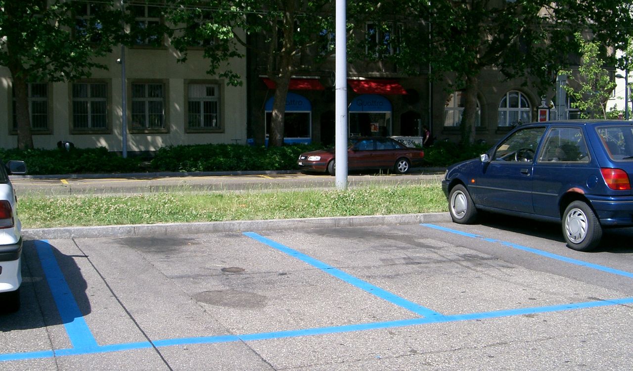 Blue-lined parking spaces with cars nearby and buildings in the background.