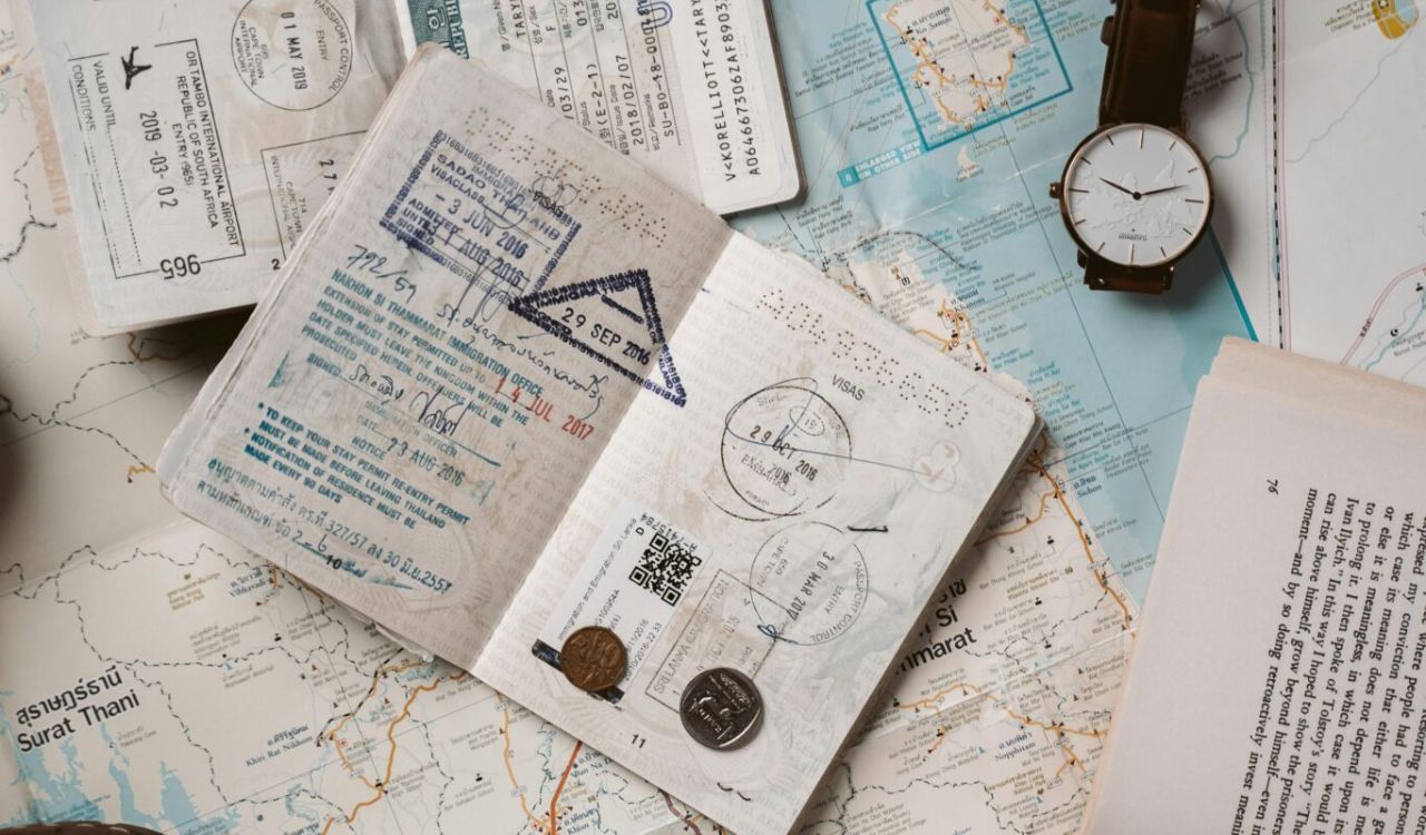 Travel essentials including passports, tickets, coins, a watch, and a book on a map