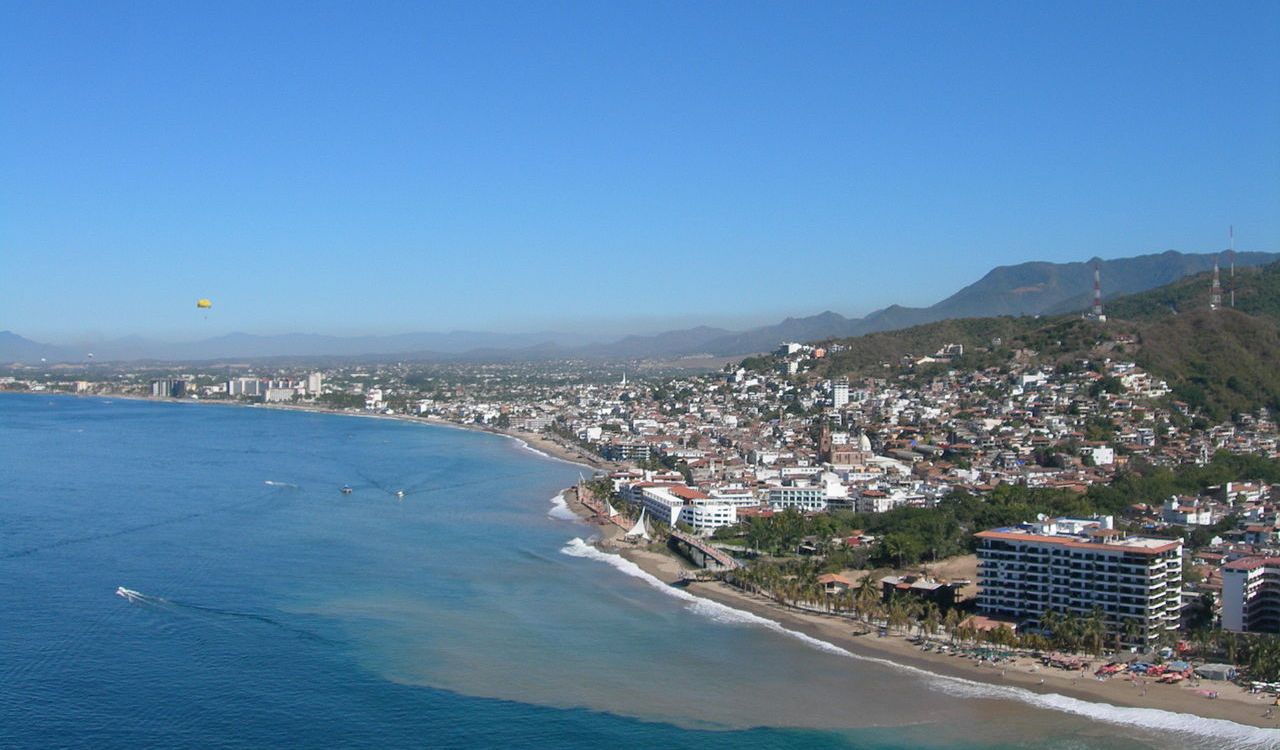 Coastal view of Puerto Vallarta with beaches, buildings, and mountains under clear blue skies