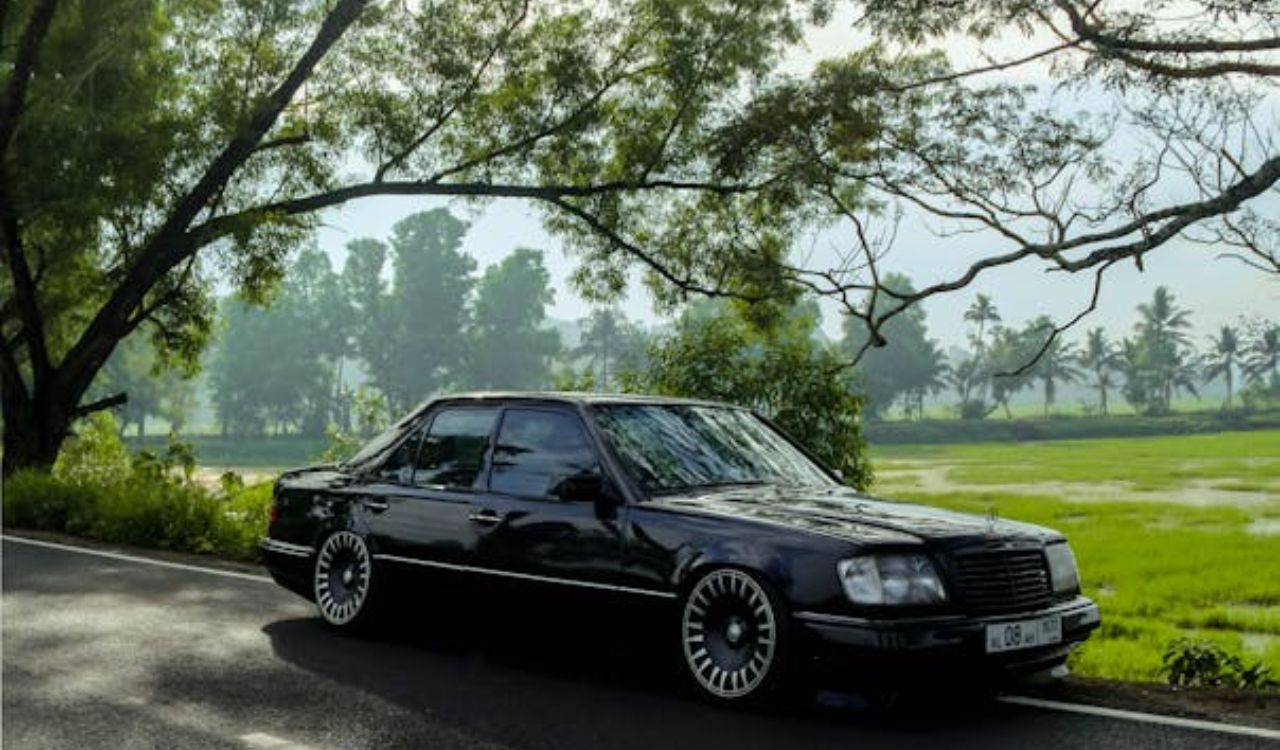 Black car parked on a scenic road near green fields and trees