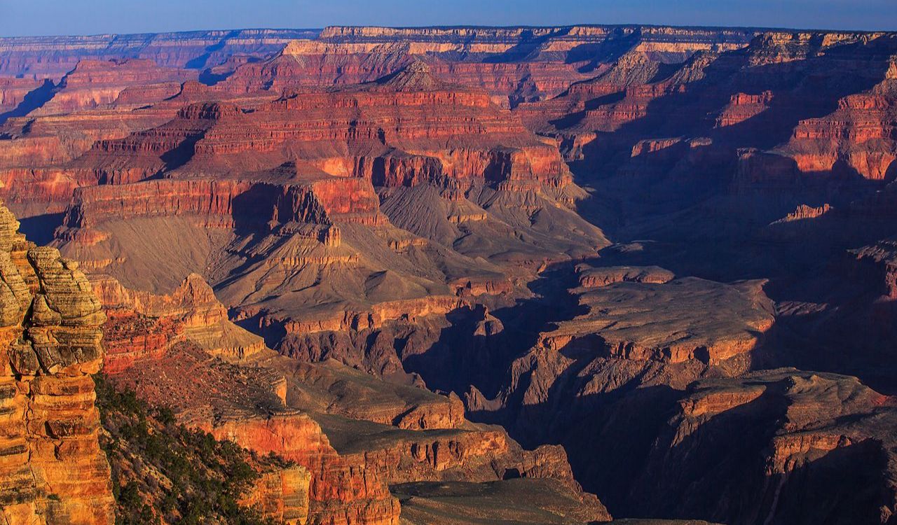 Wide view of the Grand Canyon’s layered red rock cliffs and deep valleys under a clear blue sky