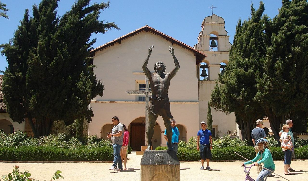 Mission San Juan Bautista with a bronze statue and visitors.