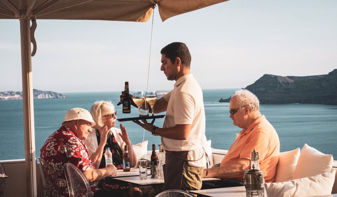 A waiter serving drinks to guests at a table with a scenic ocean view in the background
