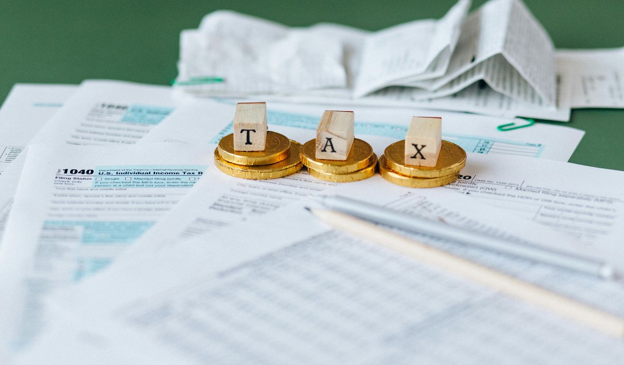 Tax documents with gold coins and wooden blocks spelling "TAX" on top.
