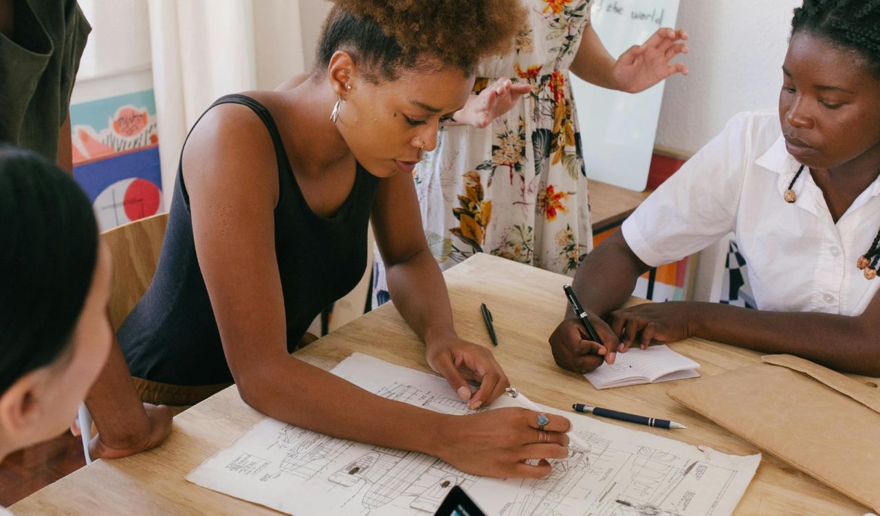 Three people discussing a blueprint and taking notes.