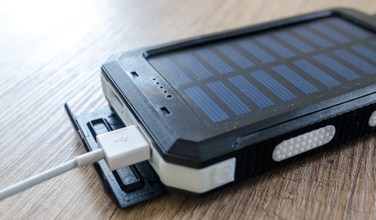A close-up of a solar-powered portable charger with a USB cable plugged into it, placed on a wooden surface