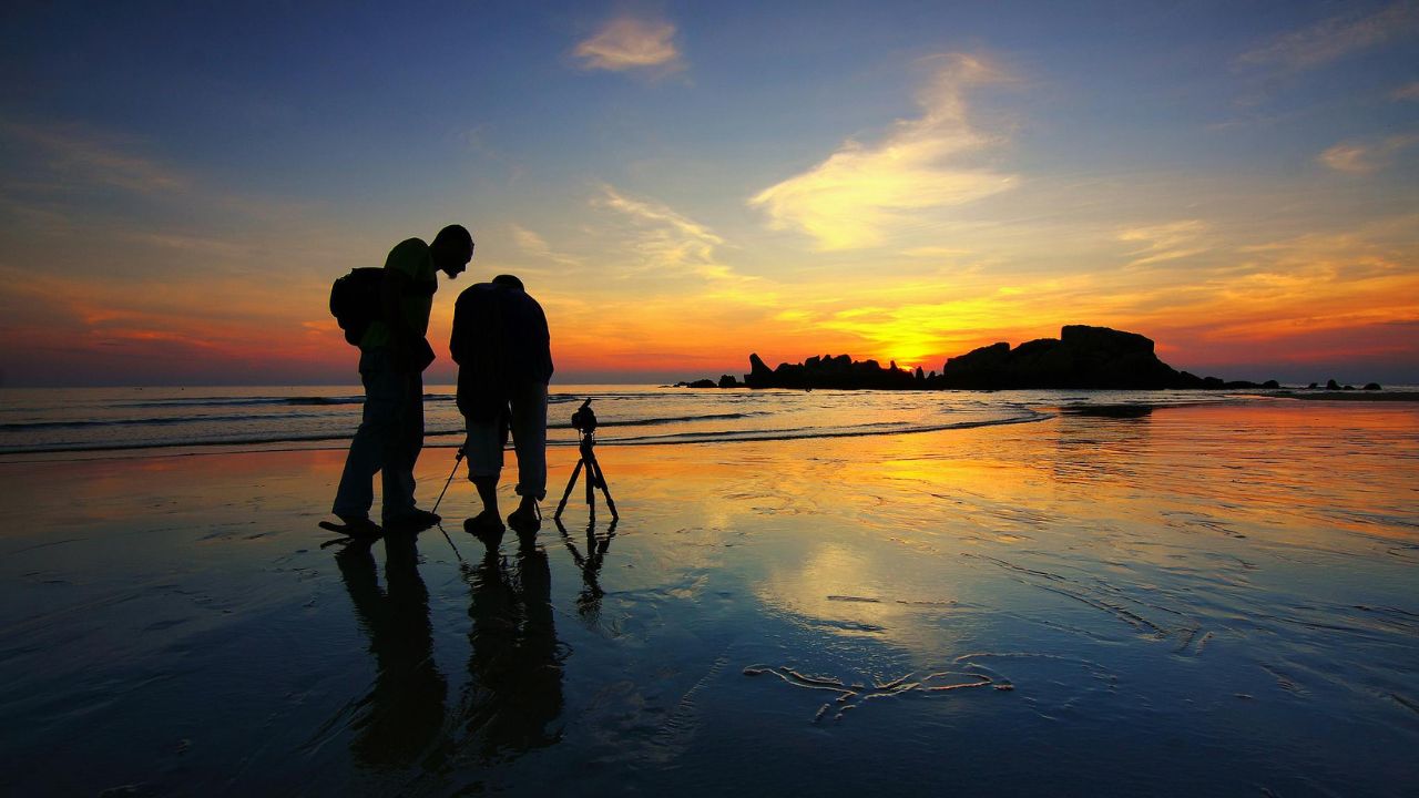 Silhouette of Two Person Taking Photo With Tripod Near Shore during Golden Hour