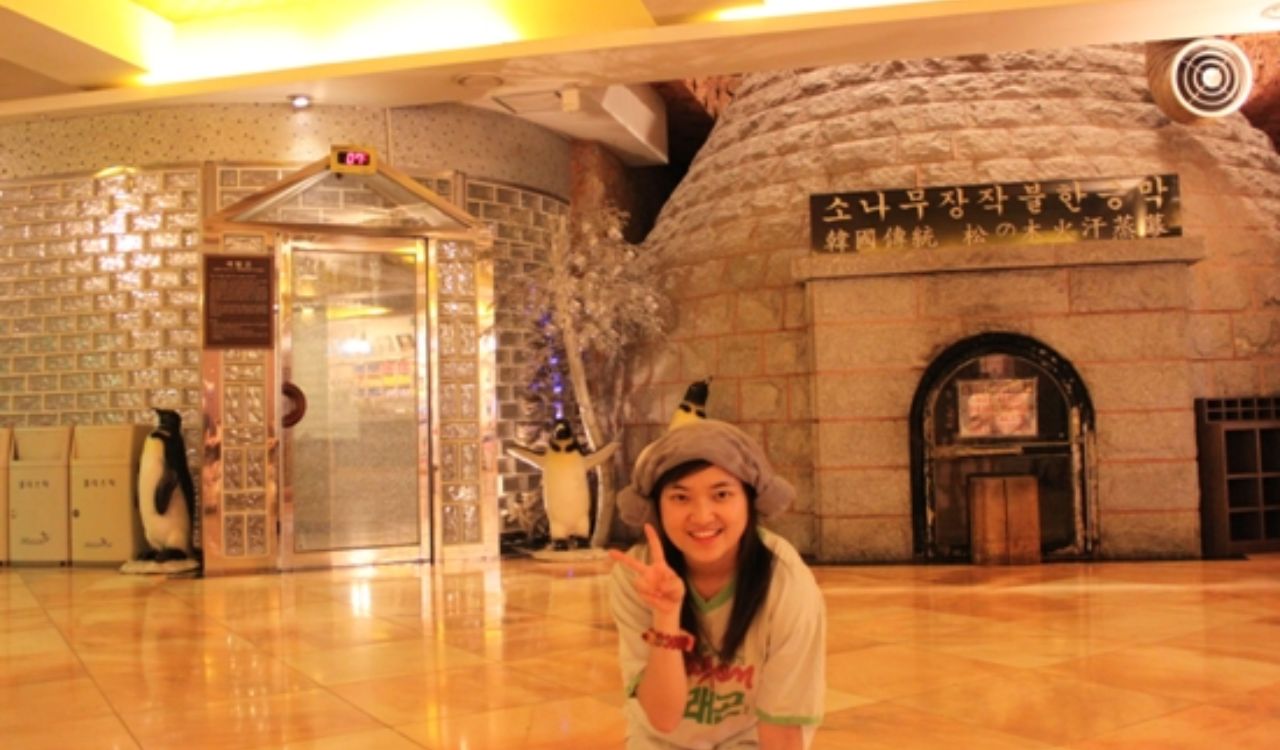 Woman posing inside a traditional Korean jjimjilbang spa with stone sauna and penguin decor
