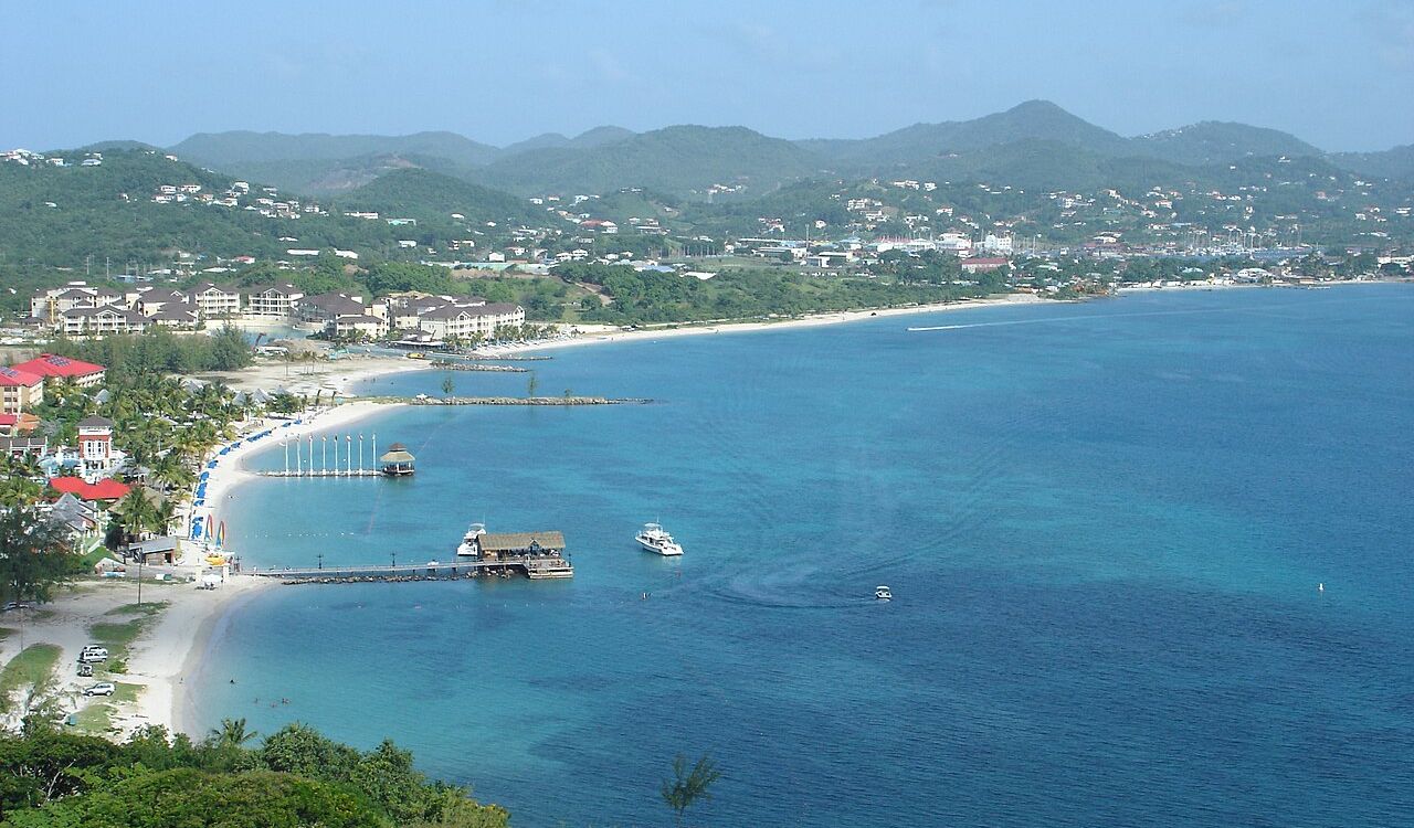 Aerial view of St. Lucia’s coastline with turquoise waters, boats, and beachside resorts nestled near lush green hills