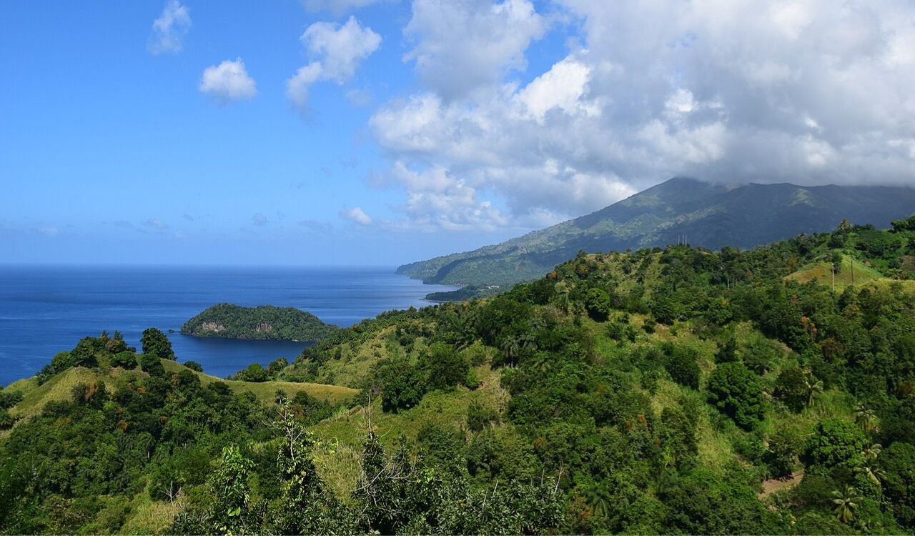 Lush green hills of St. Vincent and the Grenadines meet the deep blue sea under a partly cloudy sky