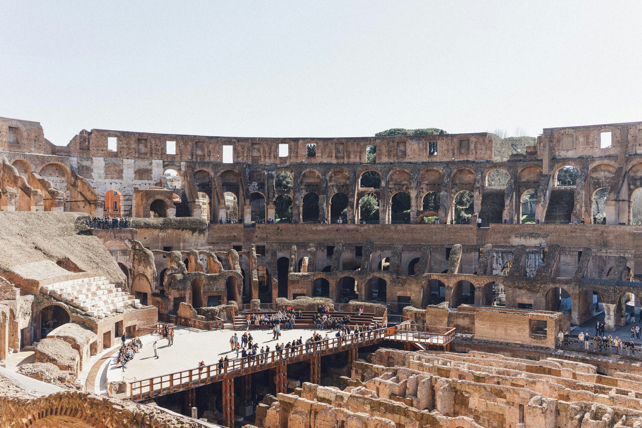 Visitors explore the interior of Rome's Colosseum, walking on platforms amid ancient stone ruins and exposed underground passages.