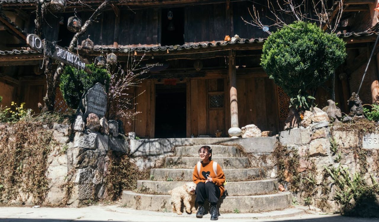 Traveler sitting outside a rustic homestay with a dog in front