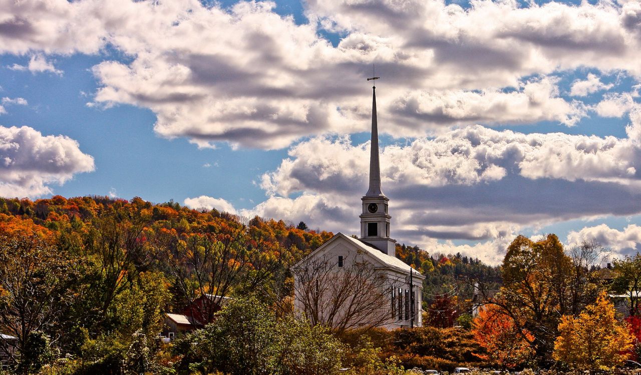 White church with a tall steeple surrounded by vibrant fall foliage in Stowe, Vermont