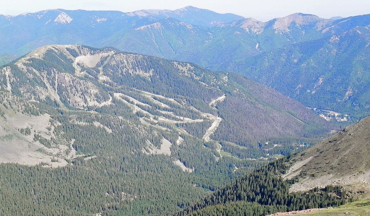 Taos Ski Valley, New Mexico, displays winding ski runs carved through dense pine forests with mountain ranges stretching into the distance