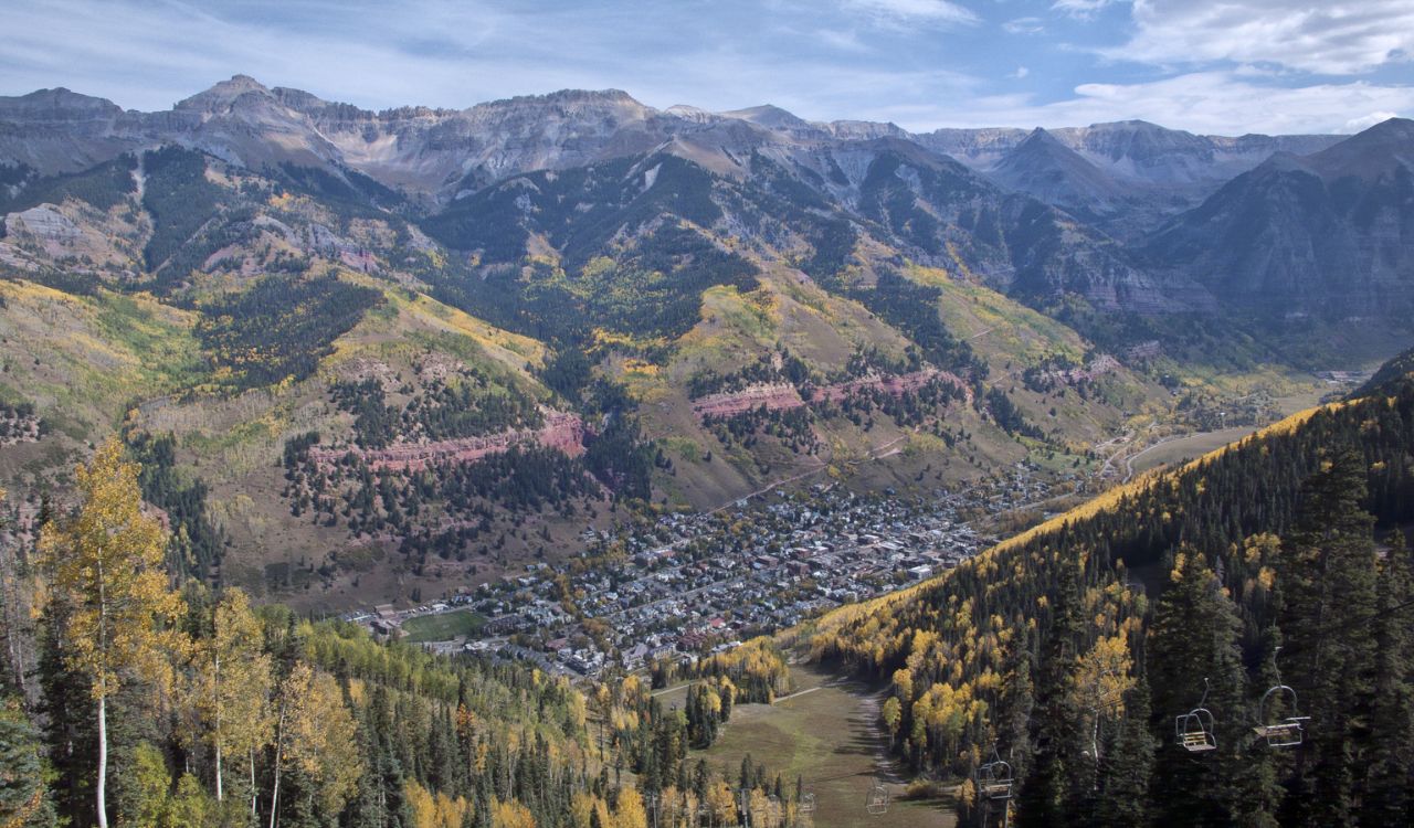 A cozy town nestled in a valley, surrounded by colorful fall trees and rugged mountain peaks in Telluride, Colorado