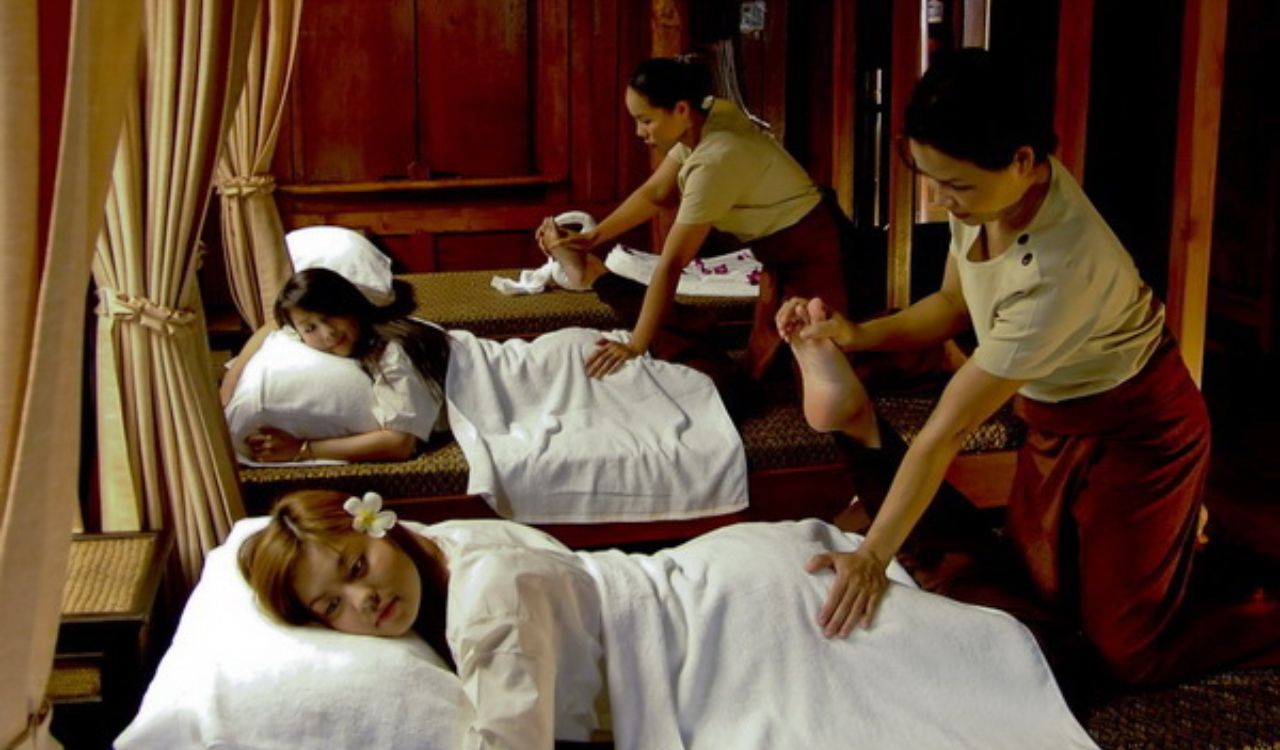 Women receiving traditional Thai massages in a serene wooden spa setting with therapists performing stretching techniques