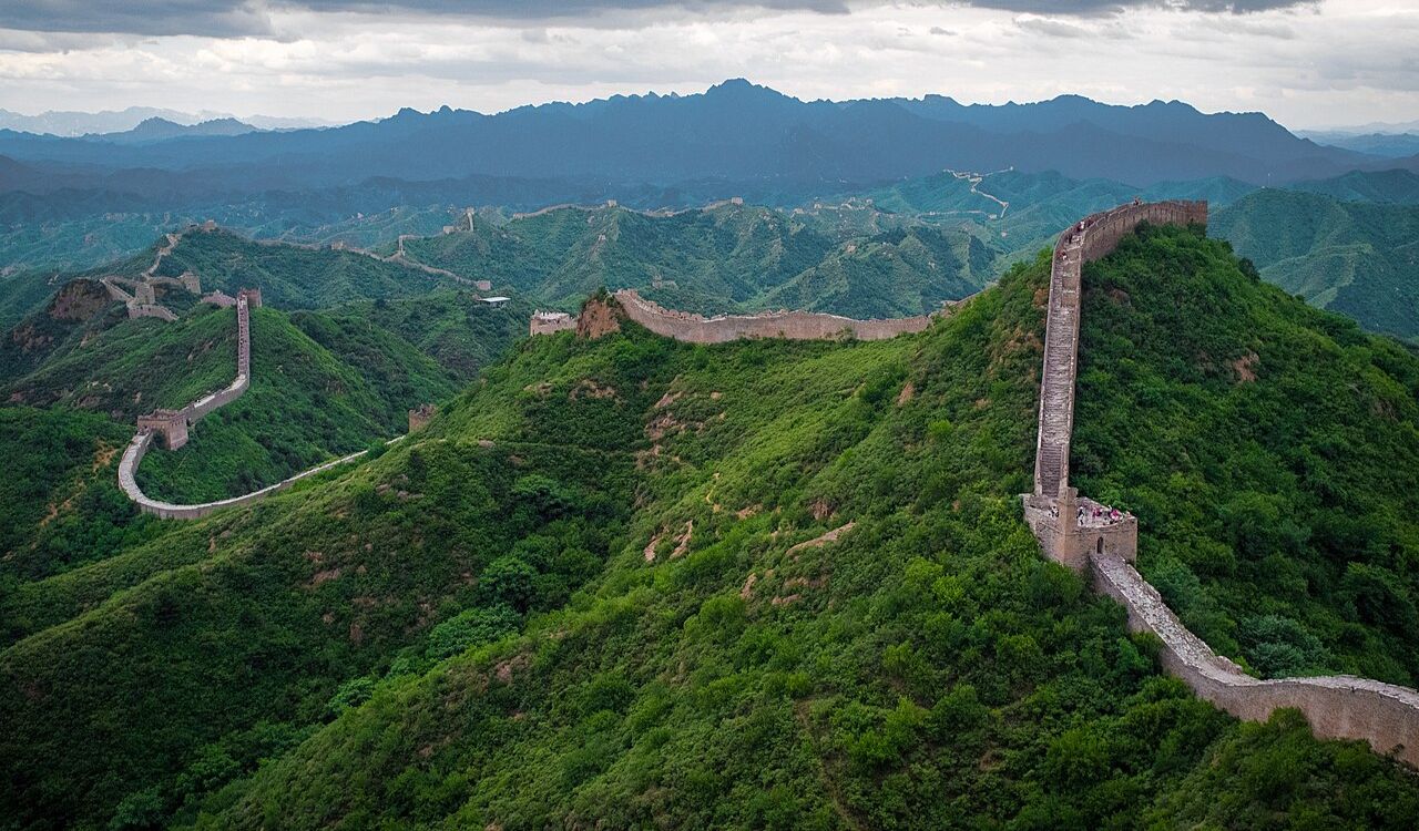 The Great Wall of China winding over lush green mountains under cloudy skies