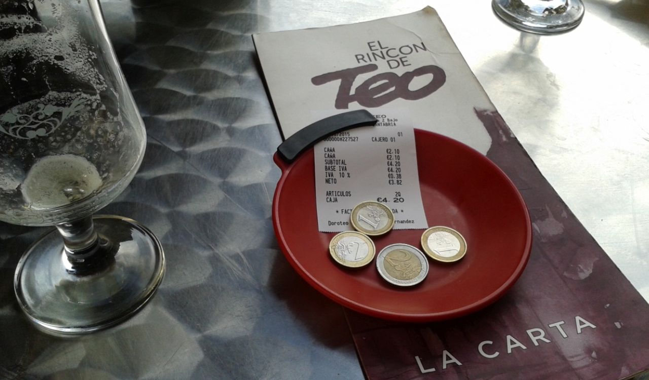 Restaurant bill with euro coins on a red tray next to an empty glass.