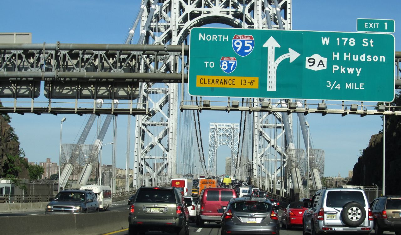 Heavy traffic on a bridge under a highway sign for I-95, I-87, and Route 9A.