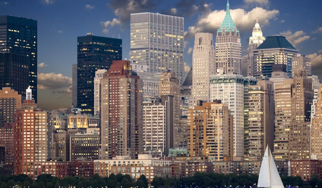 New York City skyline at sunset with high-rise buildings and a sailboat on the water