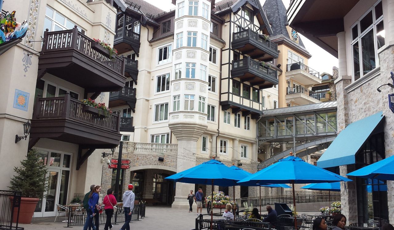 Vail, Colorado, features charming alpine-style architecture with wooden balconies, cobblestone paths, and colorful umbrellas dotting a lively village plaza
