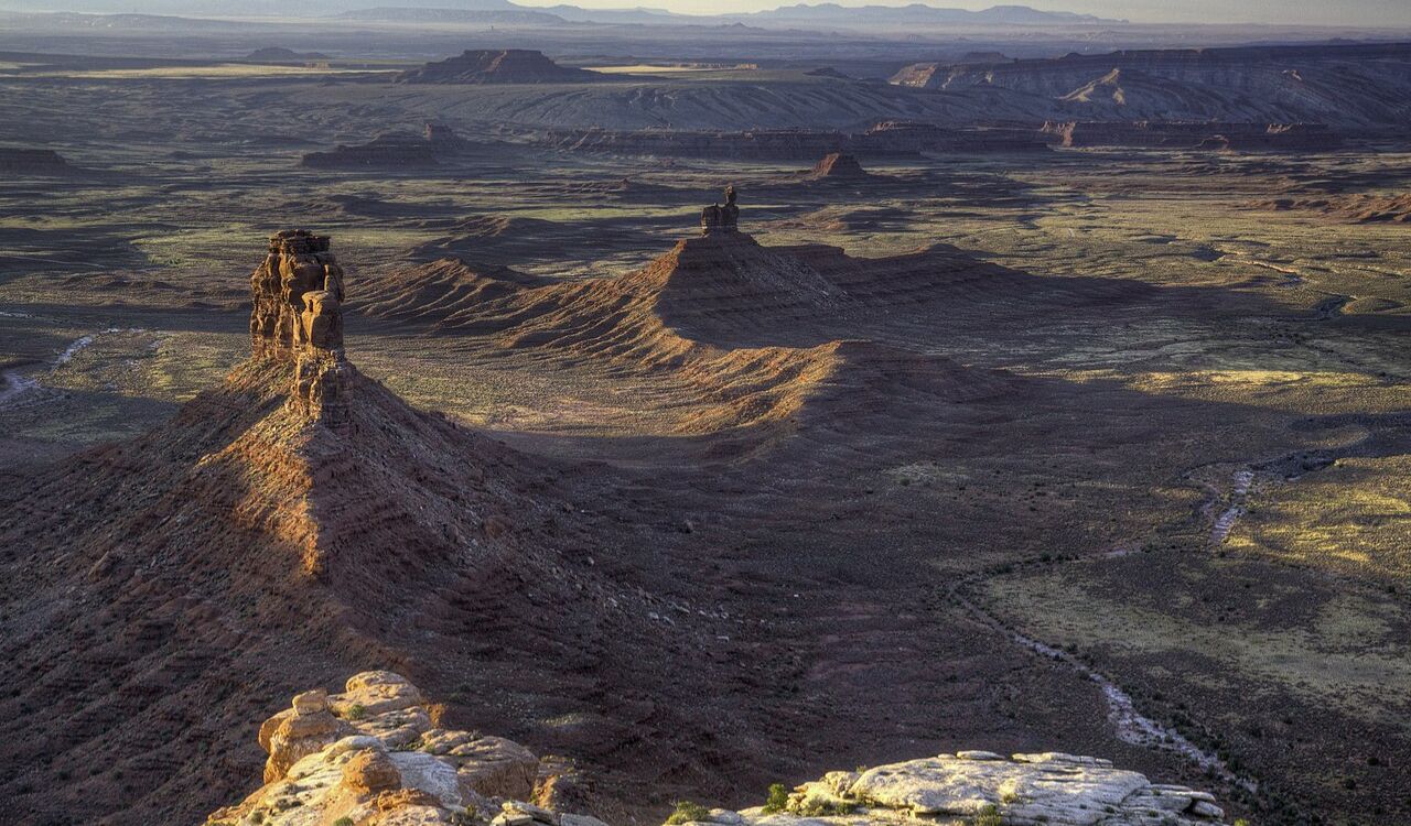 Dramatic rock formations rise from the desert floor in Valley of the Gods, Utah, under soft evening light
