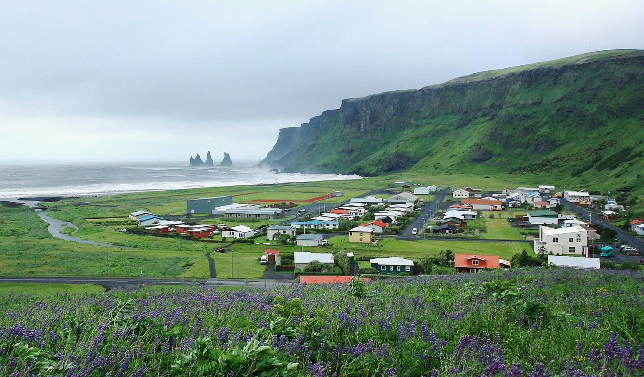 Coastal village of Vik, Iceland with lush green cliffs and Reynisdrangar sea stacks