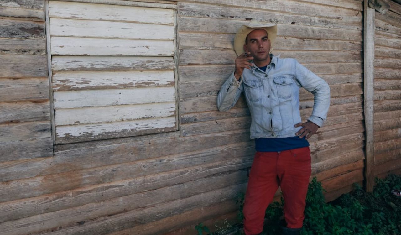 Man in cowboy hat leans on wooden wall, smoking