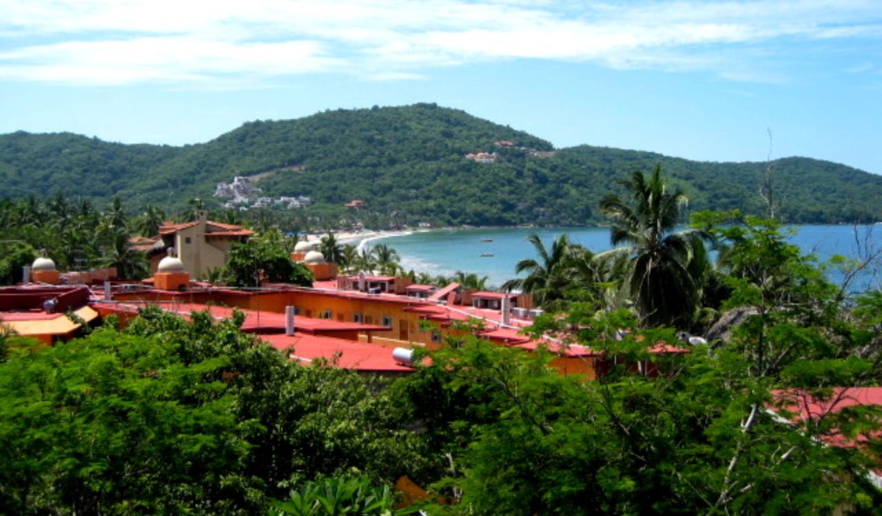 Lush green hills, a quiet beach cove, and red-roofed villas in Zihuatanejo, Mexico