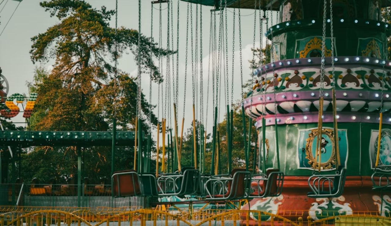 A vintage swing ride at an amusement park with colorful lights and empty seats, set against a scenic backdrop.