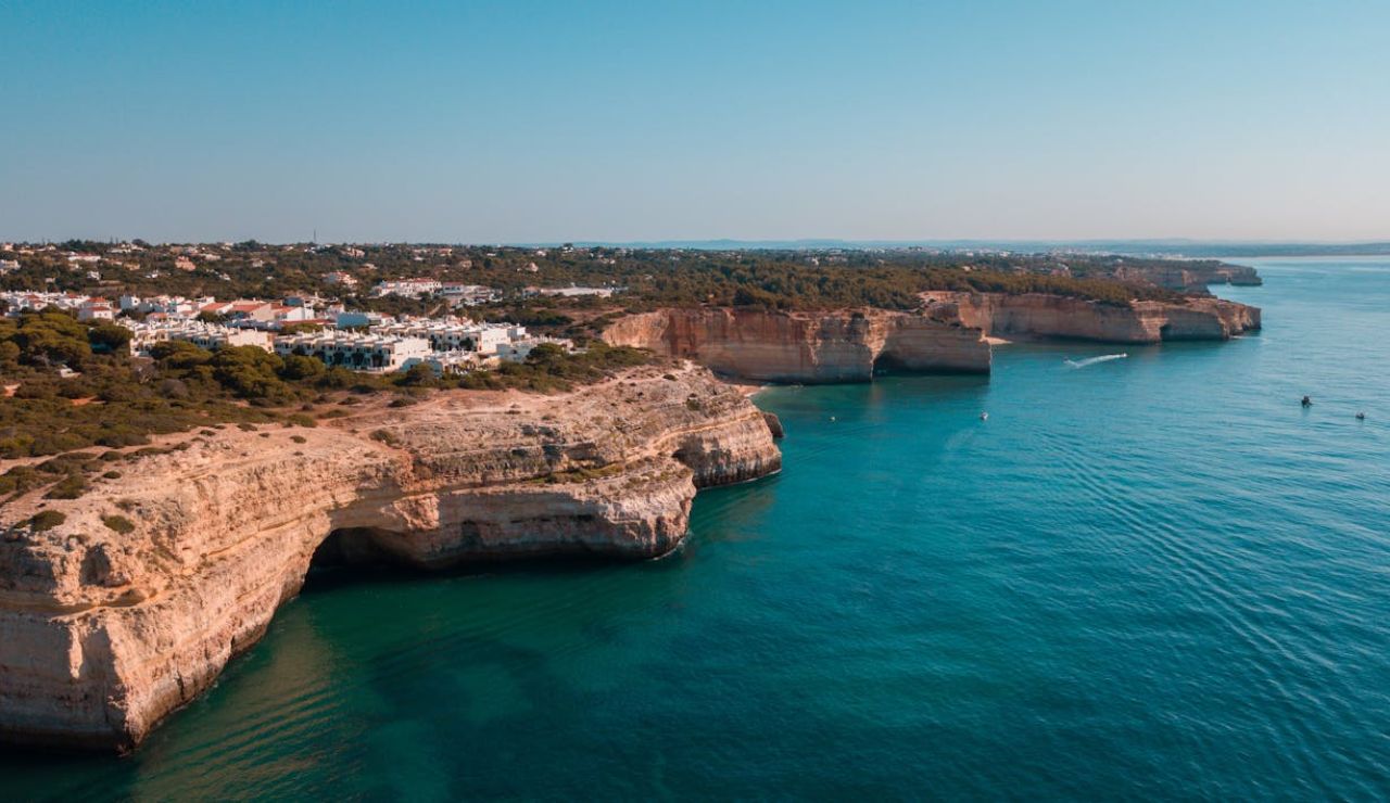 Whitewashed buildings line the cliffs of Algarve, Portugal, overlooking turquoise waters and dramatic sea caves.