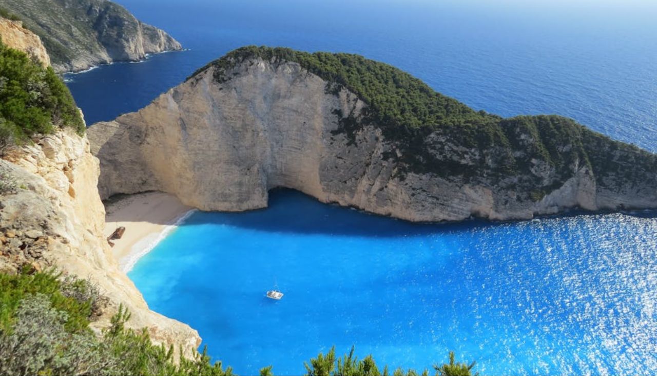 Aerial view of Navagio Beach in Greece with turquoise water, white sand, and steep cliffs surrounding a hidden cove.
