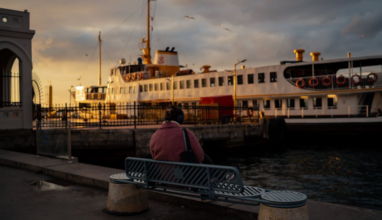 Person sitting on a bench at sunset near a docked passenger ferry.