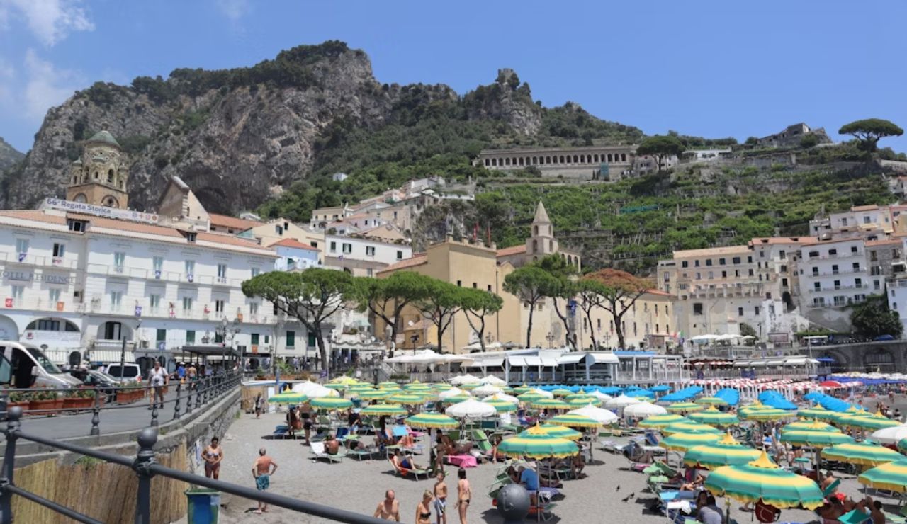 Colorful umbrellas and sunbathers on the beach in Amalfi, Italy with hillside buildings in the background.