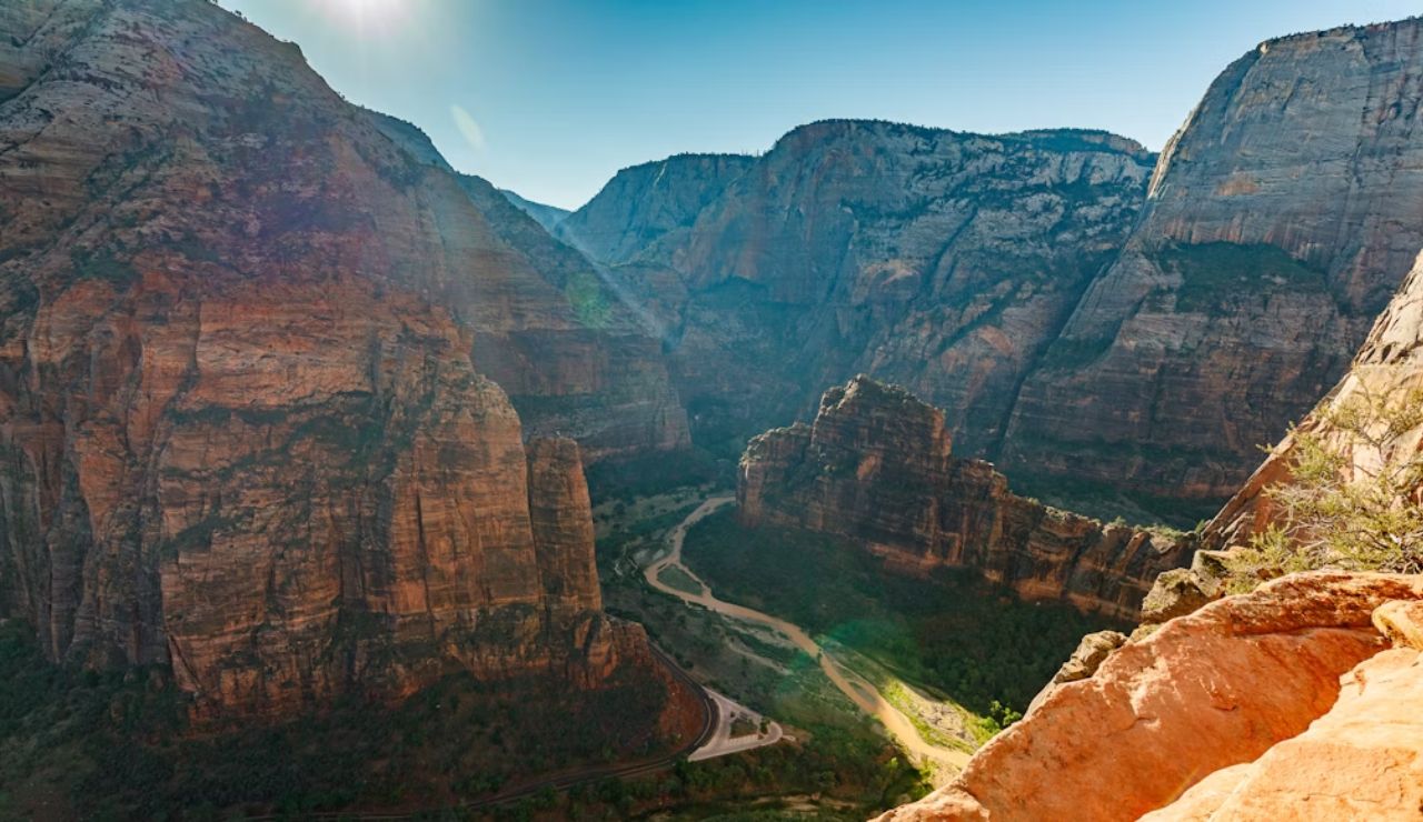 Panoramic view of Zion Canyon with towering red rock cliffs and a winding river far below, seen from a high vantage point in Zion National Park.