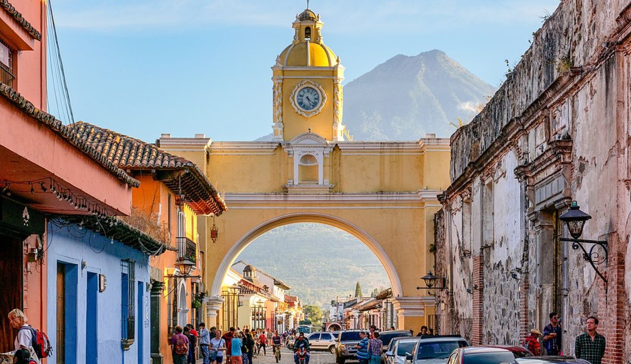 Colorful street scene in Antigua, Guatemala, featuring the iconic yellow Santa Catalina Arch with a volcano in the background.