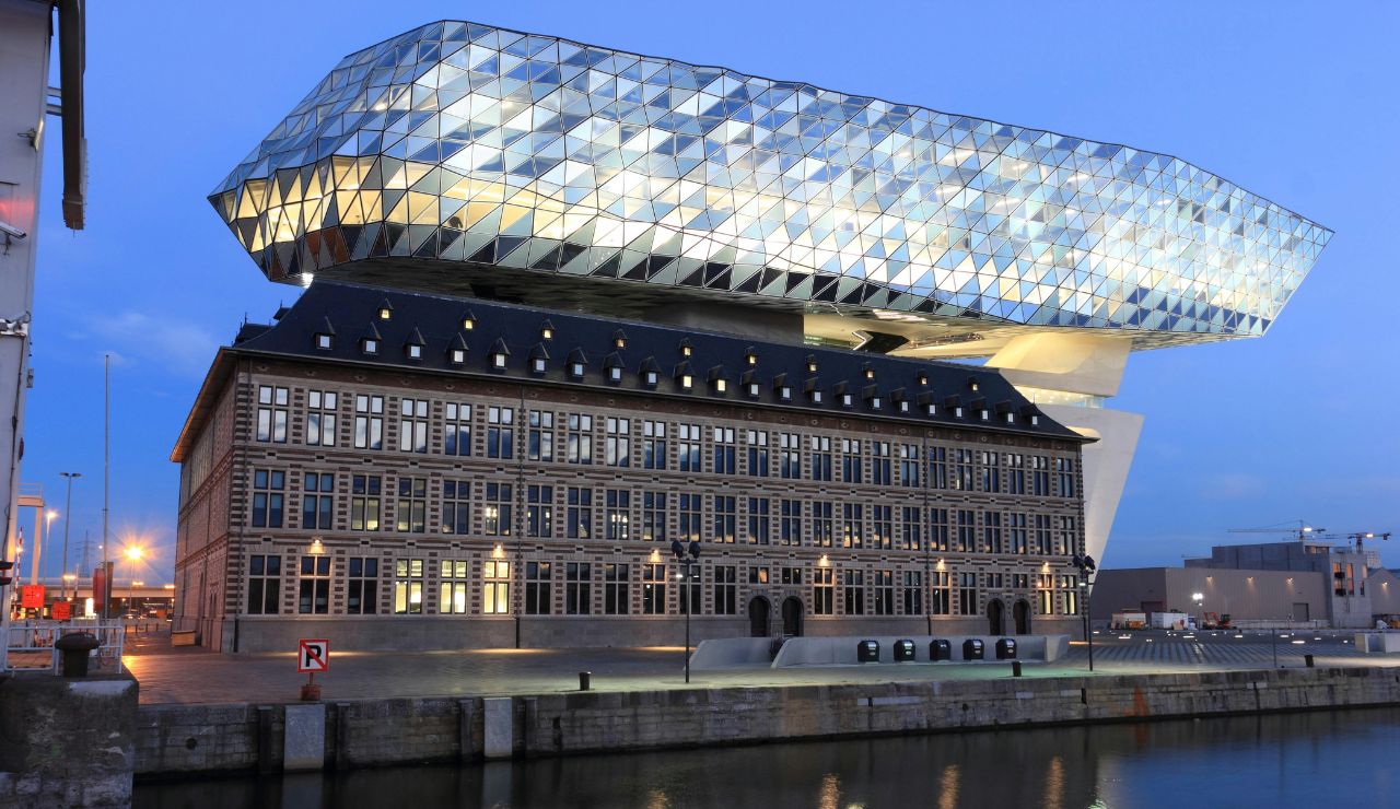 Modern glass structure of the Port House in Antwerp, Belgium, built atop a historic fire station near the waterfront at dusk.