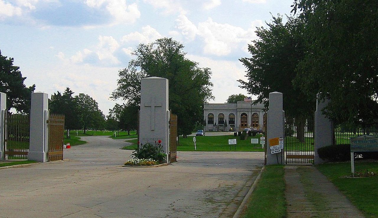 Entrance gate to a cemetery with a chapel or mausoleum in the background.