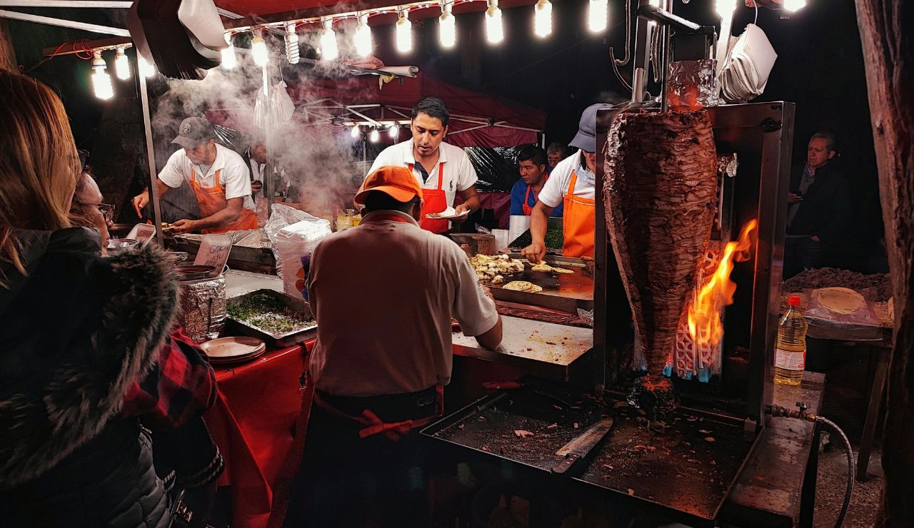Street food vendors preparing tacos al pastor at a night market.