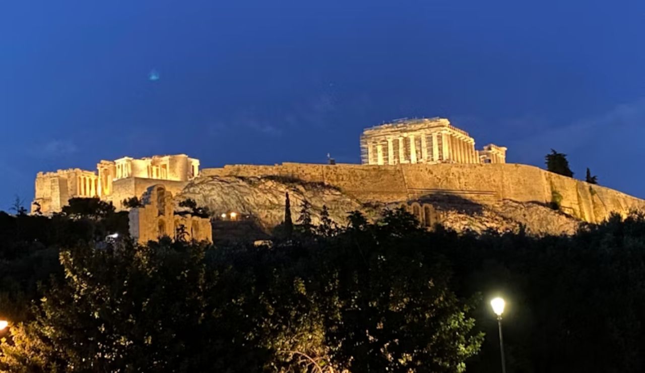 Night view of the illuminated Acropolis in Athens, Greece, with the Parthenon prominently lit atop the rocky hill.
