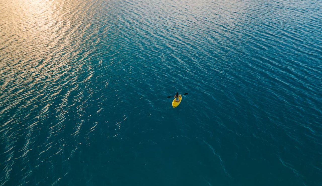 A lone kayaker paddles through calm, deep blue waters at sunset.